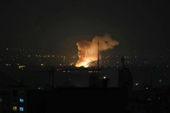 A nighttime explosion illuminates the skyline, billowing smoke against a backdrop of city lights.